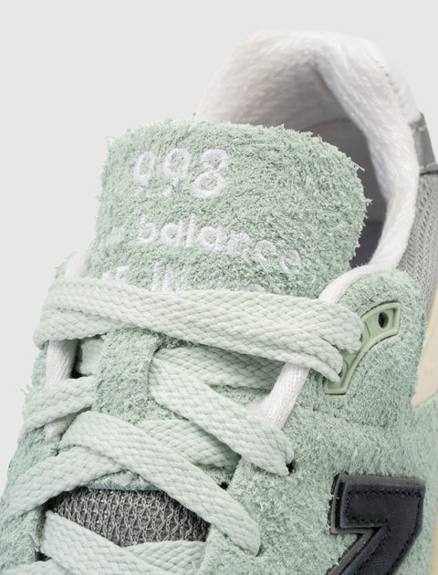 Close-up of mint green suede sneaker, textured tongue, woven laces, and side patch logo