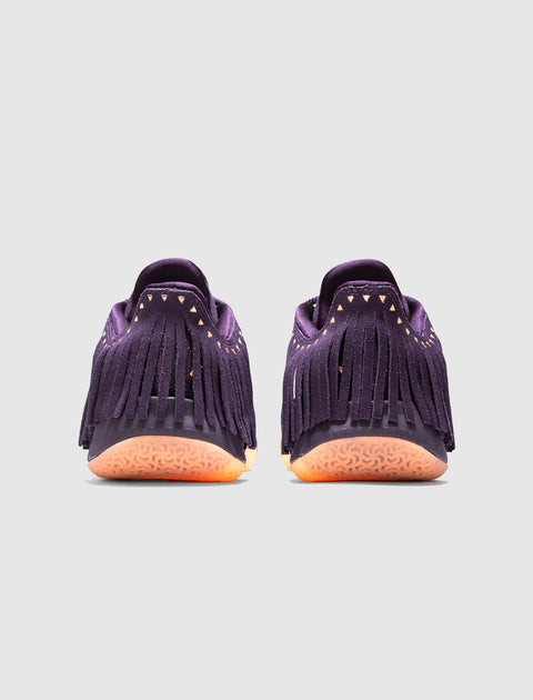 Purple suede sneakers with fringe and orange textured soles, rear view on white background
