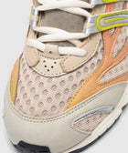 Close-up of beige mesh sneaker with orange and yellow accents, white laces, and textured toe