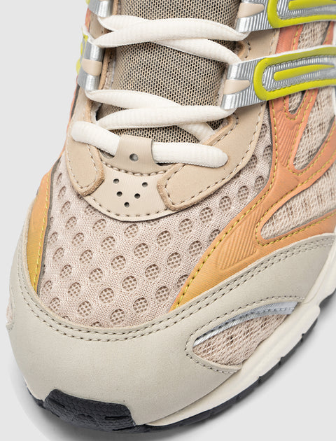 Close-up of beige mesh sneaker with orange and yellow accents, white laces, and textured toe