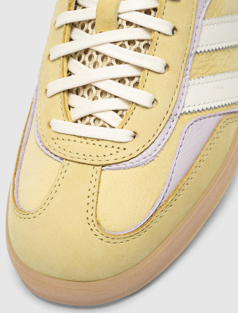 Closeup of yellow suede sneaker with mesh tongue, white laces, and lilac accents