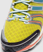 Yellow mesh sneaker closeup with blue laces, black toe cap, and orange accent details