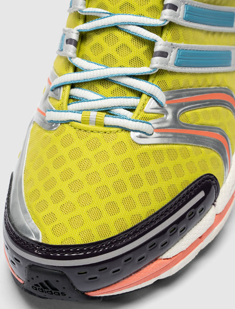 Yellow mesh sneaker closeup with blue laces, black toe cap, and orange accent details