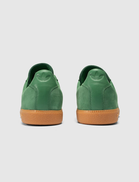 Back view of green suede sneakers with gum rubber soles on a light background