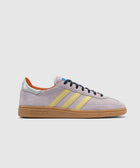 Lilac suede sneaker with yellow stripes, gum sole, silver heel tab, and black laces