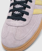 Close-up of lilac suede sneaker with black laces, mesh tongue, yellow stripes, gum sole