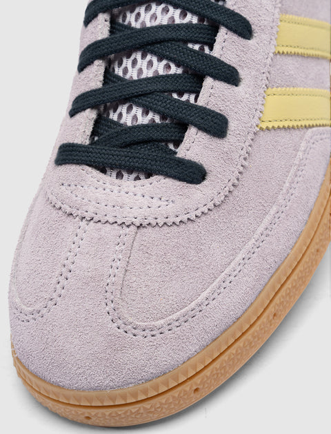 Close-up of lilac suede sneaker with black laces, mesh tongue, yellow stripes, gum sole