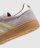 Close-up of lilac suede sneaker with yellow stripes, gum sole, and retro style details