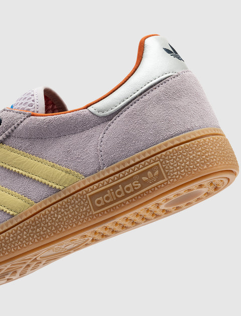 Close-up of lilac suede sneaker with yellow stripes, gum sole, and retro style details