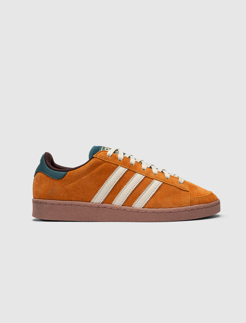 Orange suede low-top sneaker with cream stripes, teal heel accent, and brown sole on white background