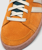 Close-up of orange suede sneaker with white laces and cream side stripes