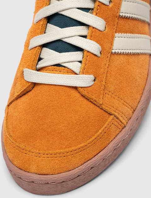 Close-up of orange suede sneaker with white laces and cream side stripes