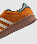 Close-up of brown suede sneaker with white stripes, teal heel tab, and textured sole