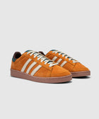 Orange suede low-top sneakers with cream stripes and brown soles on a white background.