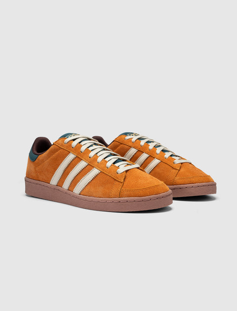 Orange suede low-top sneakers with cream stripes and brown soles on a white background.