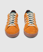 Pair of orange suede Adidas sneakers with cream stripes and rubber soles on a plain background
