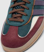 Close-up of a multicolor suede sneaker with navy, burgundy, and purple stripes detail