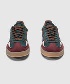 Pair of suede low-top sneakers in teal, navy, and burgundy with gum soles on white background
