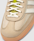 Closeup of beige suede sneaker with cream stripes, gum sole, and yellow mesh tongue detail