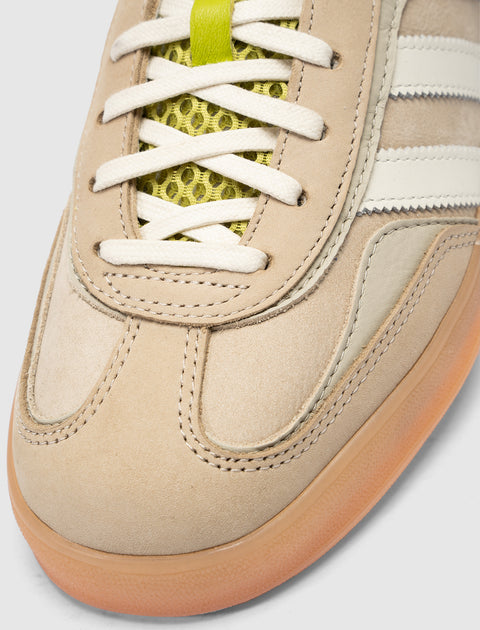 Closeup of beige suede sneaker with cream stripes, gum sole, and yellow mesh tongue detail