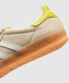 Beige suede sneaker with white stripes, gum sole, and yellow heel accent, close-up view.