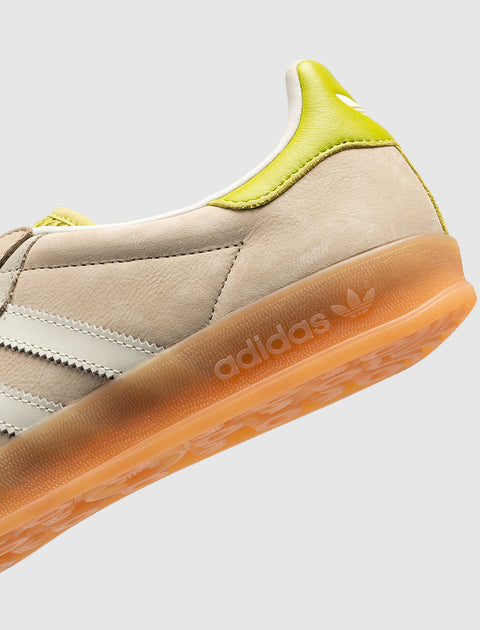 Beige suede sneaker with white stripes, gum sole, and yellow heel accent, close-up view.