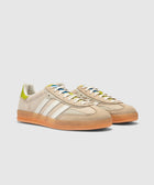 Beige and green suede low-top sneakers with gum sole and white side stripes, studio background