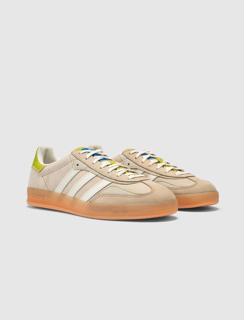 Beige and green suede low-top sneakers with gum sole and white side stripes, studio background