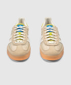 Cream and green low-top sneakers with gum soles, white stripes, and blue tongue branding