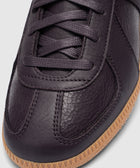 Close-up of a dark eggplant leather sneaker with textured panels and gum rubber sole