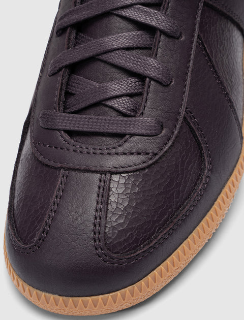 Close-up of a dark eggplant leather sneaker with textured panels and gum rubber sole
