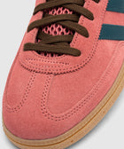 Close-up of pink suede sneaker with brown laces, blue stripes, and gum sole.