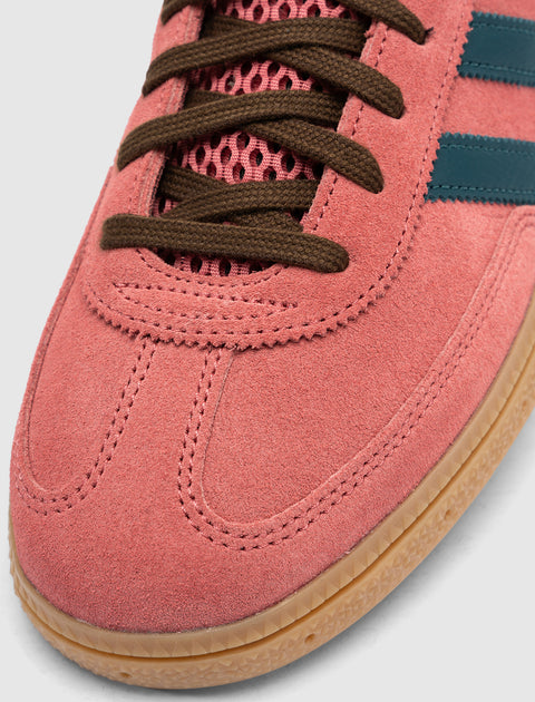 Close-up of pink suede sneaker with brown laces, blue stripes, and gum sole.