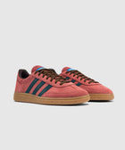 Red suede low-top sneakers with blue stripes, gum sole, and brown laces on white background