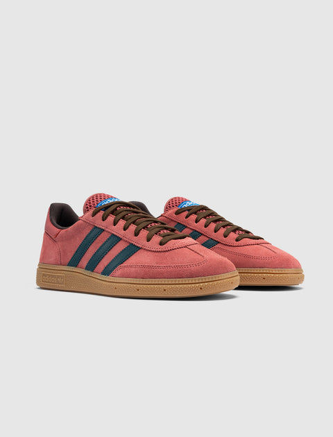 Red suede low-top sneakers with blue stripes, gum sole, and brown laces on white background