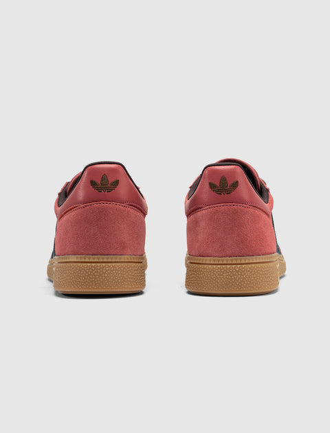 Back view red suede low-top sneakers with gum soles and black accents on white background