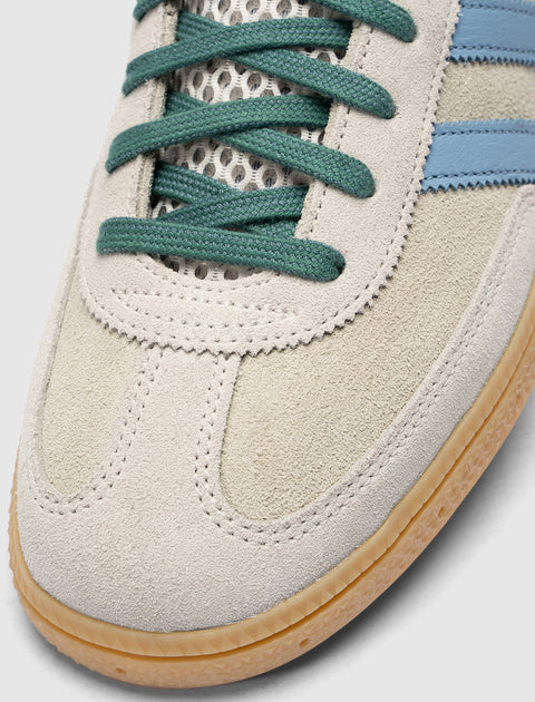 Close-up of suede sneaker with green laces, blue stripes, and gum sole.