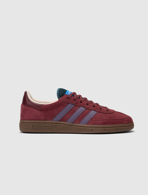 Red suede sneaker with purple stripes, brown sole, side profile on white background