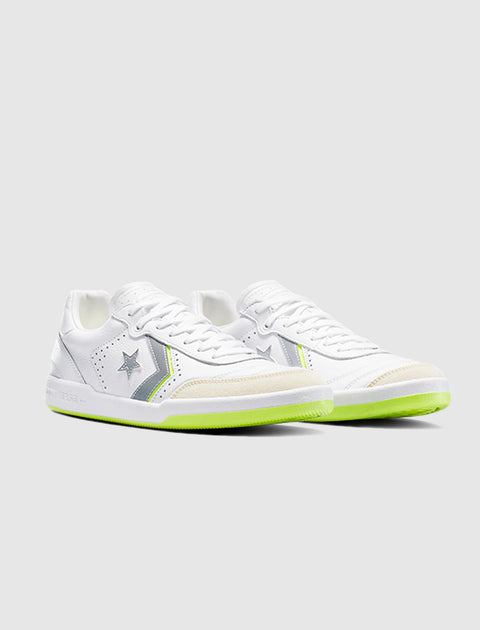 White low-top sneakers with grey star details and neon green soles on a plain background