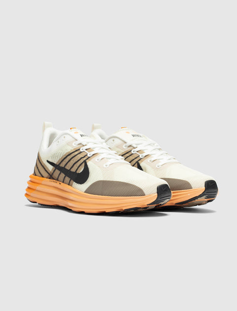 Men's white and brown sneakers with orange sole, black swoosh, modern streetwear style