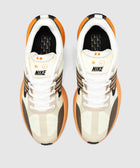 Top view of Nike sneakers in beige, brown, and orange with white laces on a gray background