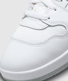 Close-up of a white sneaker with textured mesh and leather upper, white laces, and rubber sole
