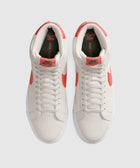 Top view of white suede high-top sneakers with orange Swoosh accents and laces