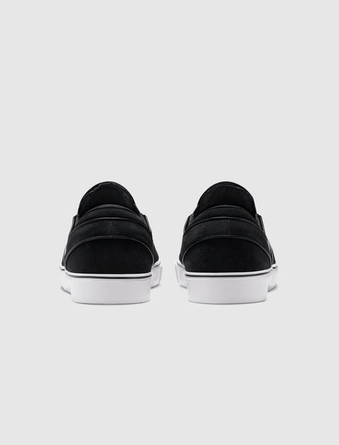 Back view of black slip-on sneakers with white soles on a plain gray background