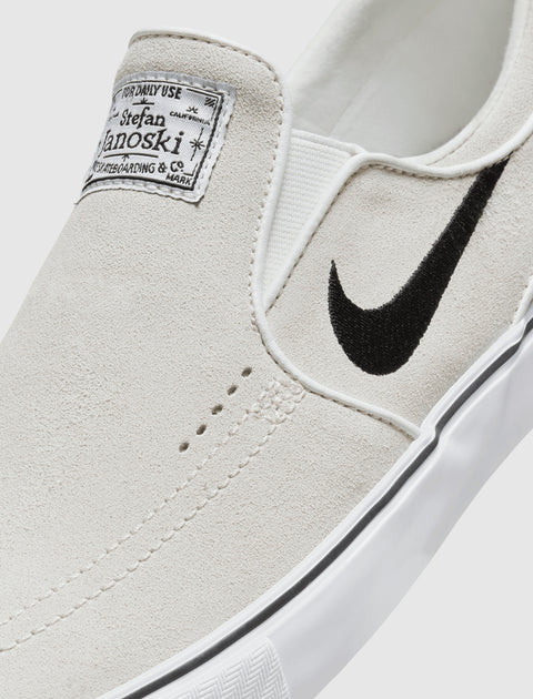 White suede slip-on skate shoe with black swoosh logo and label on tongue