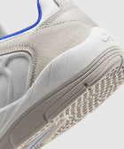 Close-up of white and beige sneaker with textured suede upper, blue trim, and rubber outsole