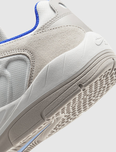Close-up of white and beige sneaker with textured suede upper, blue trim, and rubber outsole
