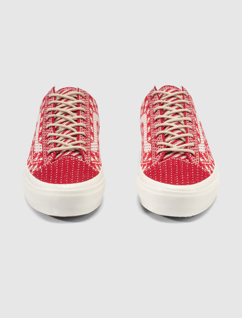 Pair of red and white patterned low-top sneakers with beige laces on a light background