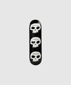 Black skateboard deck with three white skull graphics and 'pleasures' text on grey background