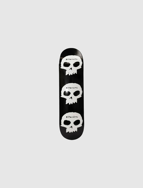 Black skateboard deck with three white skull graphics and 'pleasures' text on grey background